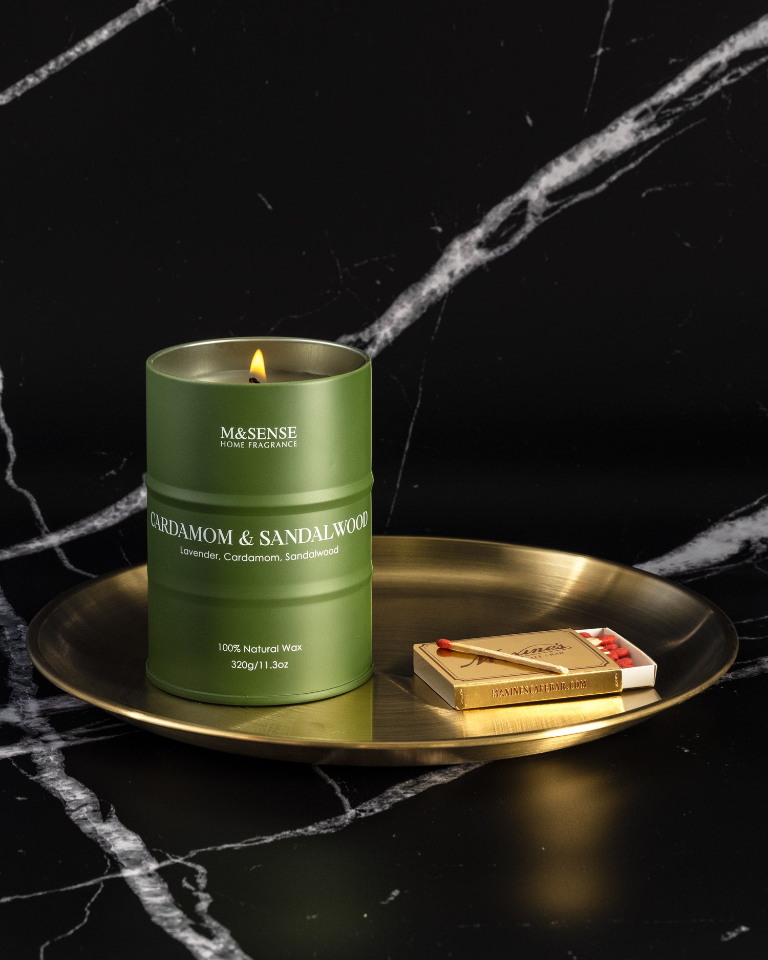 Green candle with 'M&SENSE' branding on a gold tray against a black background